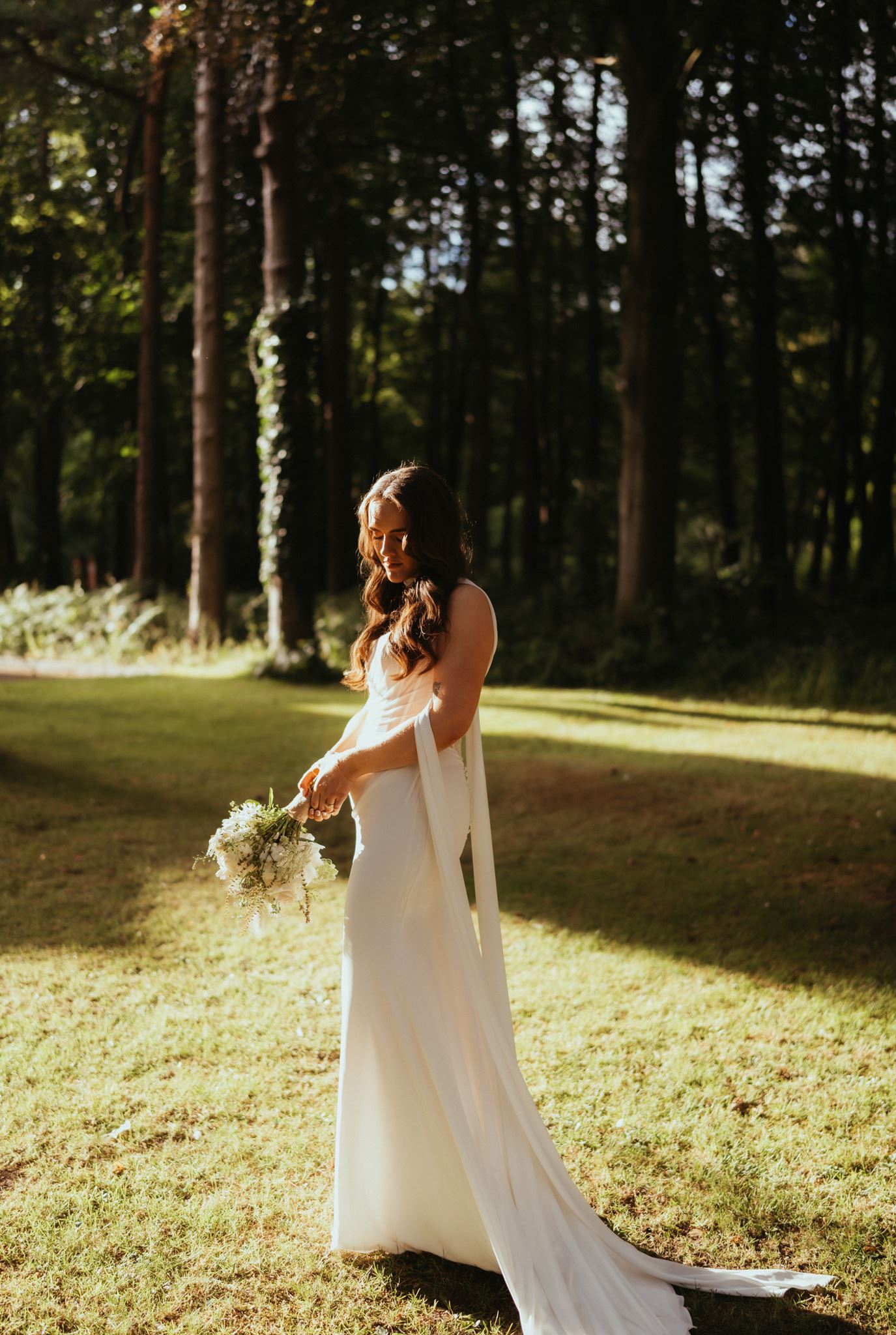 Bride in sunlit woodland holding her bouquet