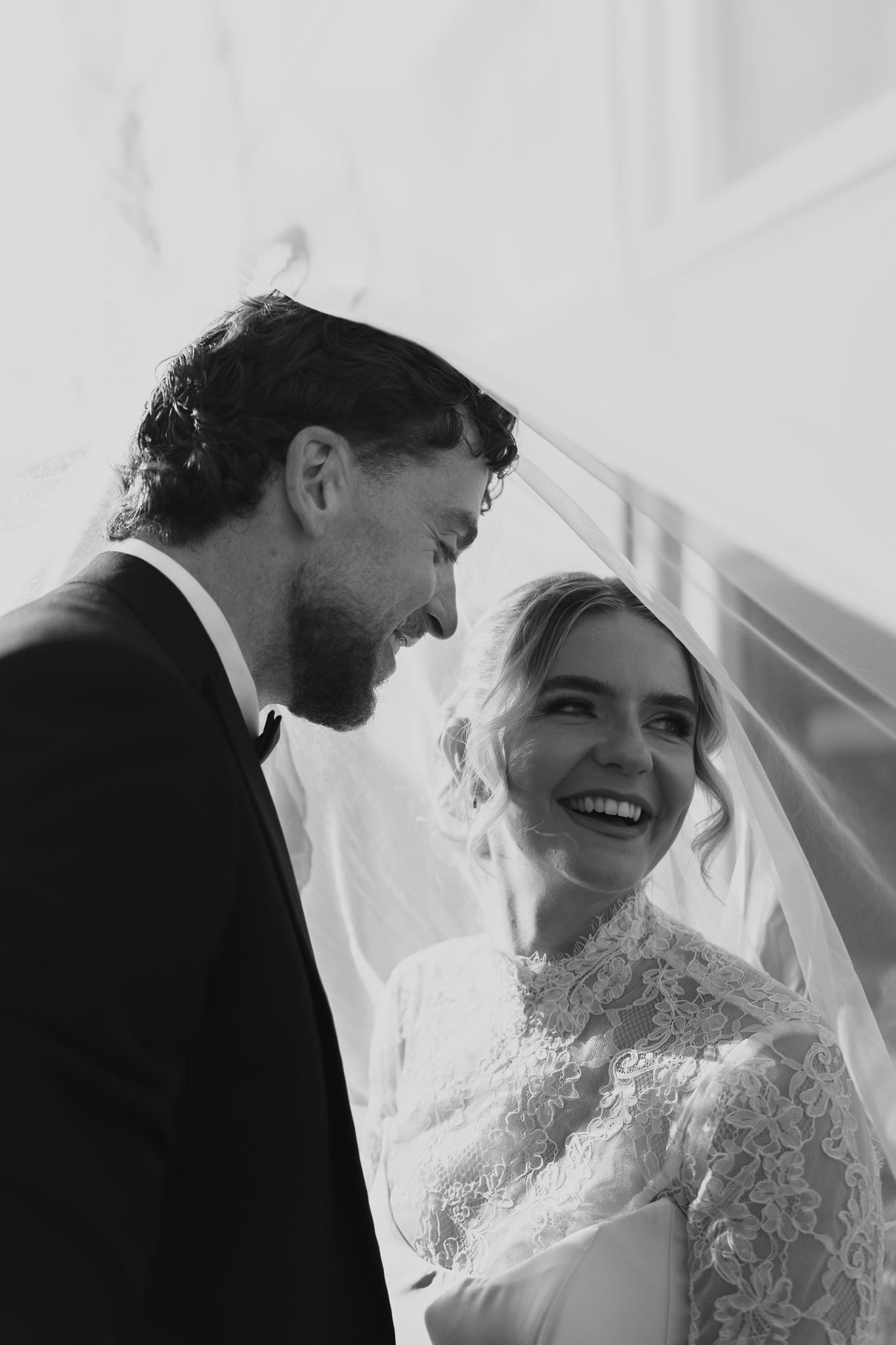 Bride laughing with her groom beneath the veil