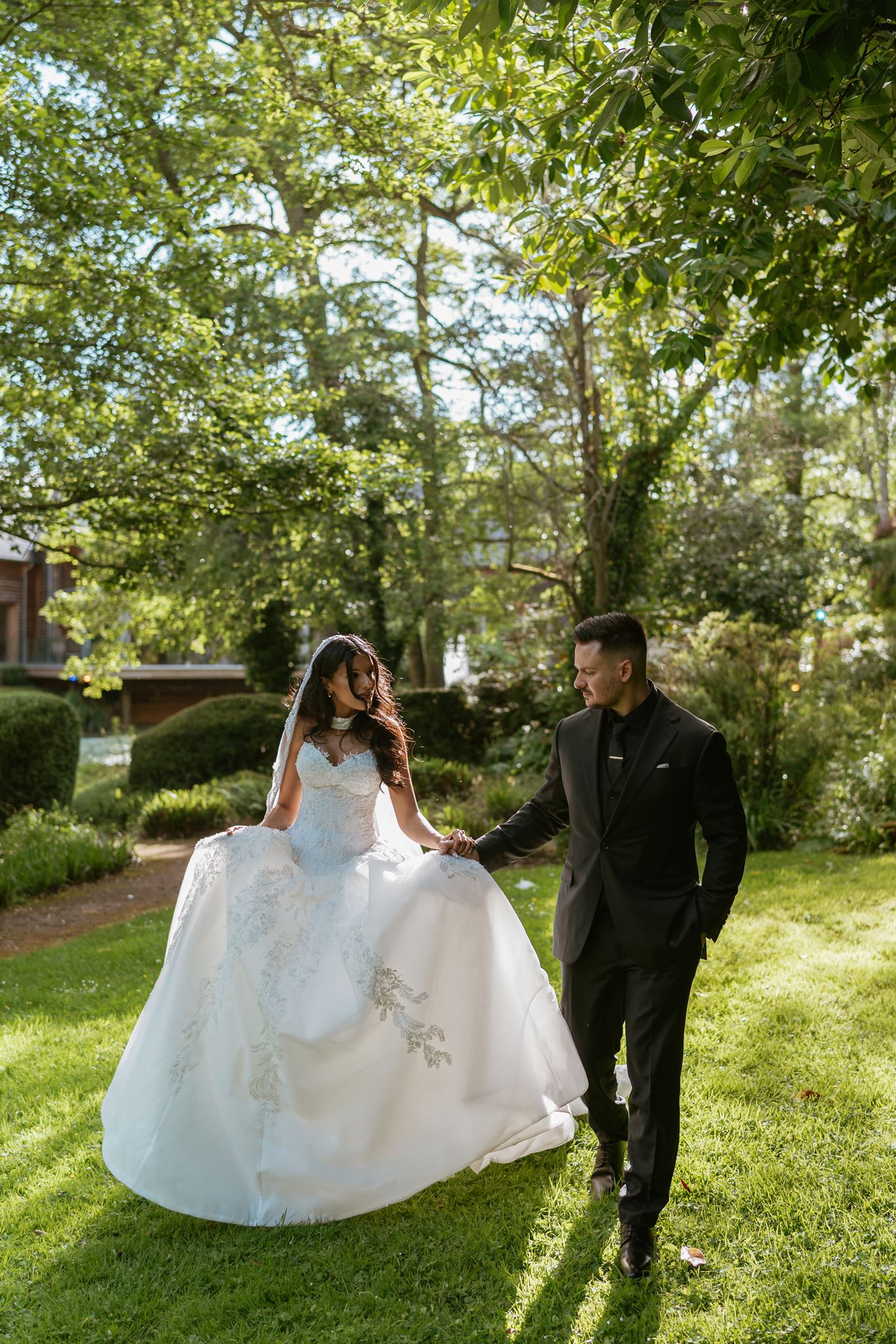 Bride and groom walking hand in hand through a sunlit garden