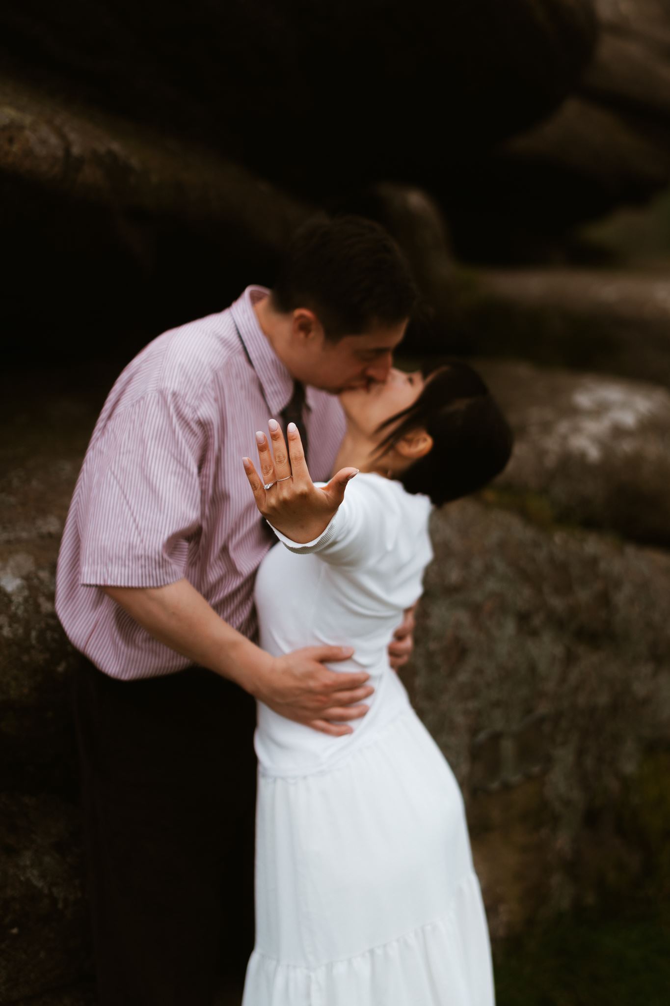 Engagement ring held to camera as the couple kiss