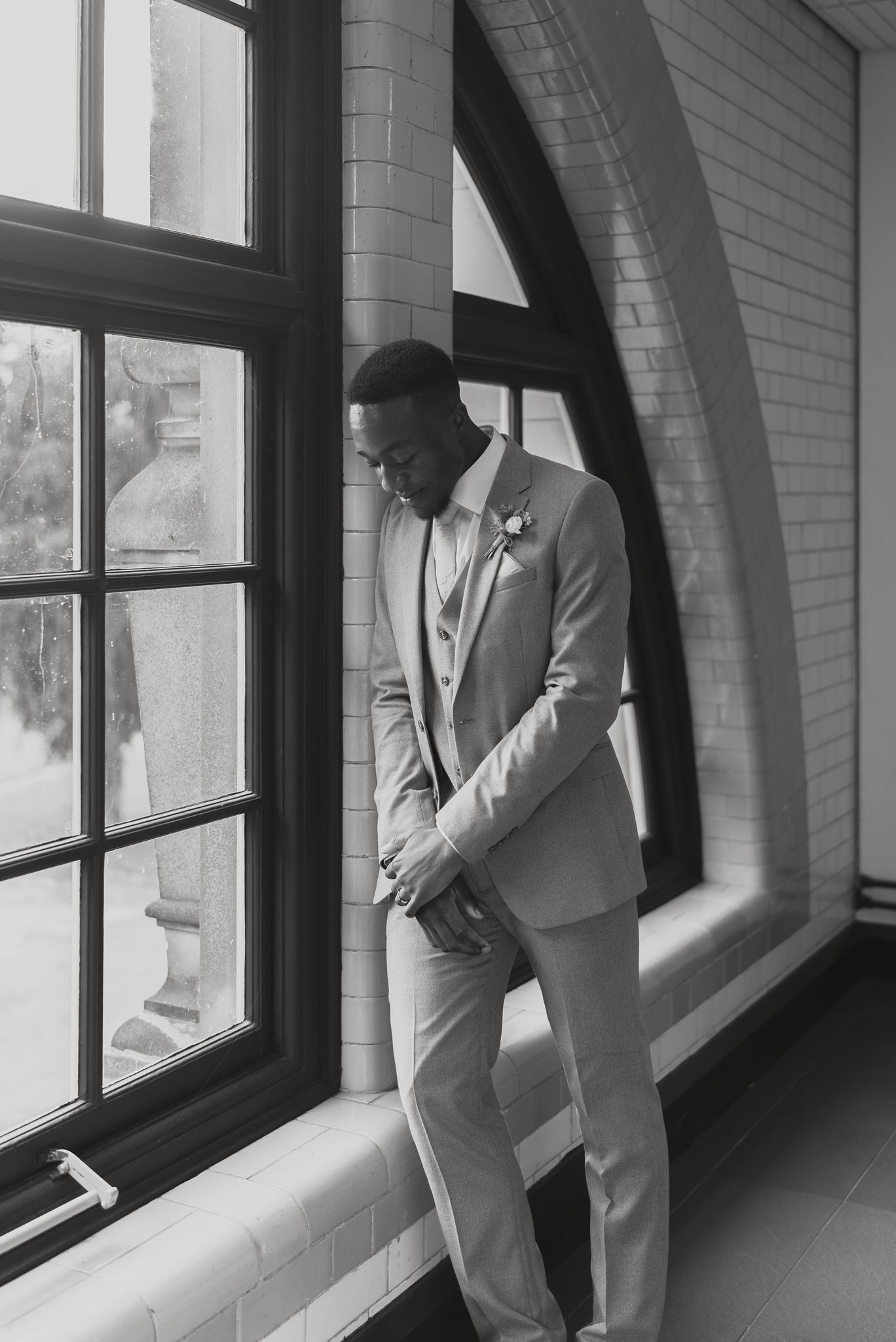 Groom waiting quietly by a tall arched window